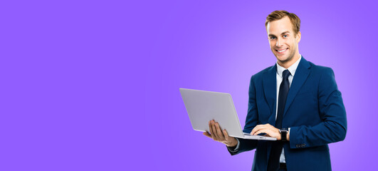 Smiling businessman in blue confident suit, working with laptop, over violet purple color background. Handsome young man at studio concept picture. Copy space.