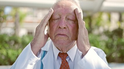 Canvas Print - Senior grey-haired man doctor suffering for headache at park