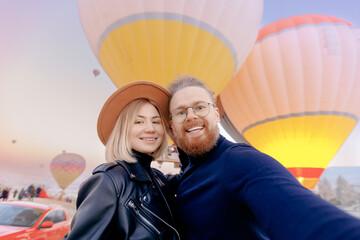 Wall Mural - Couple lovers tourist making selfie photo in Cappadocia with colorful hot air balloon with sun light. Concept banner travel Turkey Goreme