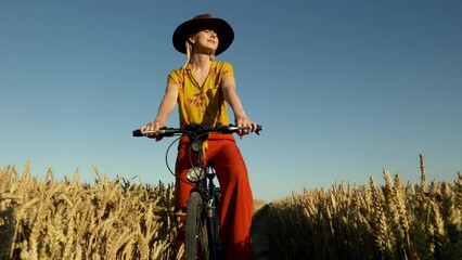 Sticker - Stylish woman in bright vintage clothes and hat on bike in golden wheat field