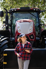 Sticker - Woman farmer with a digital tablet on the background of an agricultural tractor.