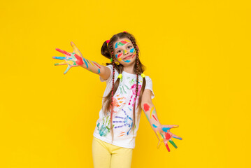 Wall Mural - Drawing and creativity for children. A little girl shows her palms painted with multicolored paints. A child smeared in paint. Yellow isolated background.