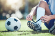 © Daniels C/peopleimages.com - Ball, man and soccer player tie shoes for training, fitness games and performance on field. Closeup, football athlete and lace sneakers on feet, grass pitch and sports competition on stadium ground