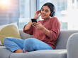© Siyavuya M/peopleimages.com - Relax, music and phone with woman on sofa and dance for streaming, social media and audio. Happy, technology and radio with person listening to headphones in living room at home for energy and sound