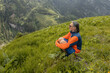 © Guzel - A long-haired gray-haired man sits on a steep green slope and enjoys a landscape view, Austria, the Alps