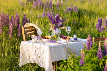 Wall Mural - Elegant gorgeous wedding table decor or romantic dinner arrangement outdoors in blooming field. Purple lupine flowers, candles, fruits and wine, wooden vintage furniture. Sunset, summer, golden hour