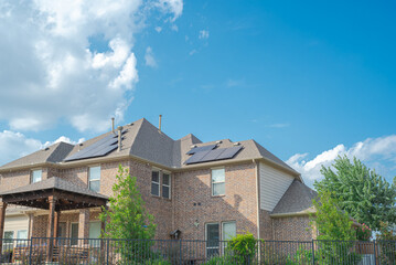 Black solar panels on shingle roofing of two story suburban residential house under sunny cloud blue sky in Flower Mound, Texas, America