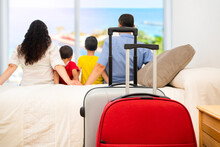 Back View Of A Family Of Tourists Relaxing Looking Through A Window In An Hotel Room After Arrival With Suitcases In The Foreground