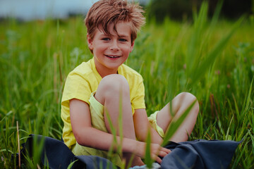 Wall Mural - Happy smiling boy sits in the green meadow on towel