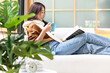 © freebird7977 - Happy young woman reading book on sofa at home.  Lifestyle freelance relax and chill drinking coffee in living room, Nature garden background.  Lifestyle Concept