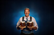 canvas print picture - Oktoberfest waiter in the traditional Bavarian suit serving beer mugs on dark blue background
