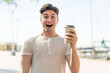 Young handsome man holding a take away coffee at outdoors with surprise and shocked facial expression