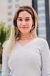 © Jose Calsina - Vertical individual portrait of one happy blonde female smiling looking at camera with friendly expression. Front view of isolated young adult employee woman standing outside. Caucasian lady posing