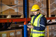 © eakgrungenerd - Male professional worker wearing safety uniform and hard hat using digital tablet inspect product on shelves in warehouse. Man worker check stock inspecting in storage logistic factory.