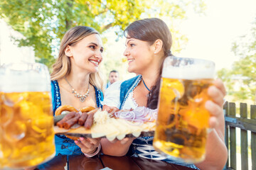 Wall Mural - Two girls in Tracht with food and drink in beer garden