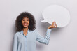 © wayhome.studio  - Horizontal shot of positive curly haired woman dressed in blue shirt smiles broadly demonstrates empty speech bubble for your advertisement isolated over white background. Place your promo here