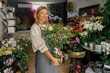 © Yaroslav Astakhov - Attractive woman flower shop owner in apron holding bouquet of flowers at florist store