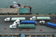 Fully loaded trucks with bags of fertilizer approaching the pier for manual discharging by stevedores and transfer cargo to barge and ship. Behind is tugboat.