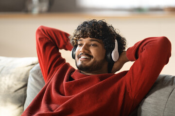 Sticker - Smiling Young Indian Man In Wireless Headphones Listening Music At Home