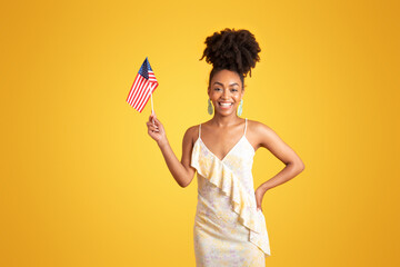 Wall Mural - Smiling millennial african american lady showing USA flag, isolated on yellow background