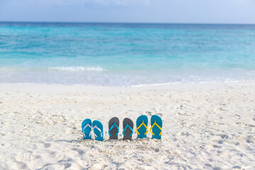 Three pairs of flip flops on the beach on the background of ocean in the Maldives. Family vacation