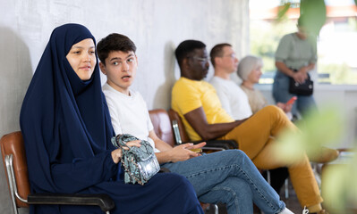 Wall Mural - Young arab woman and teenage boy waiting for their turn on chair at reception