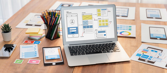 Digital and paper wireframe designs for web or mobile app UI UX display on laptop computer screen. Panoramic shot of developer workspace for brainstorming and design application framework. Scrutinize