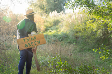 young woman with a hat in an environment of trees and sun with a wooden sign that says think green to protect the natural environment and take care of the environment