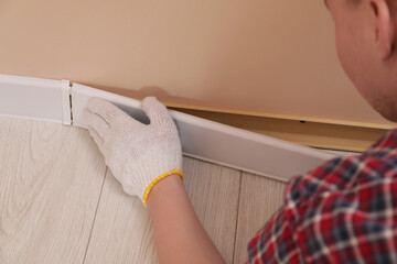 Sticker - Man installing plinth on laminated floor in room, closeup