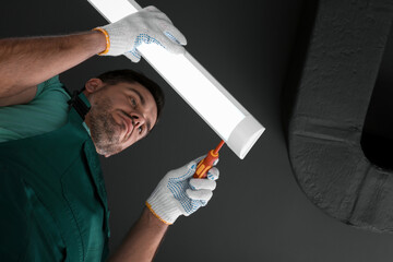 Poster - Ceiling light. Electrician installing led linear lamp indoors, bottom view