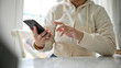 © bongkarn - Close-up image of a woman using her smartphone at a table in a minimal coffee shop.