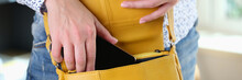 Woman hand putting smartphone in yellow leather crossbody