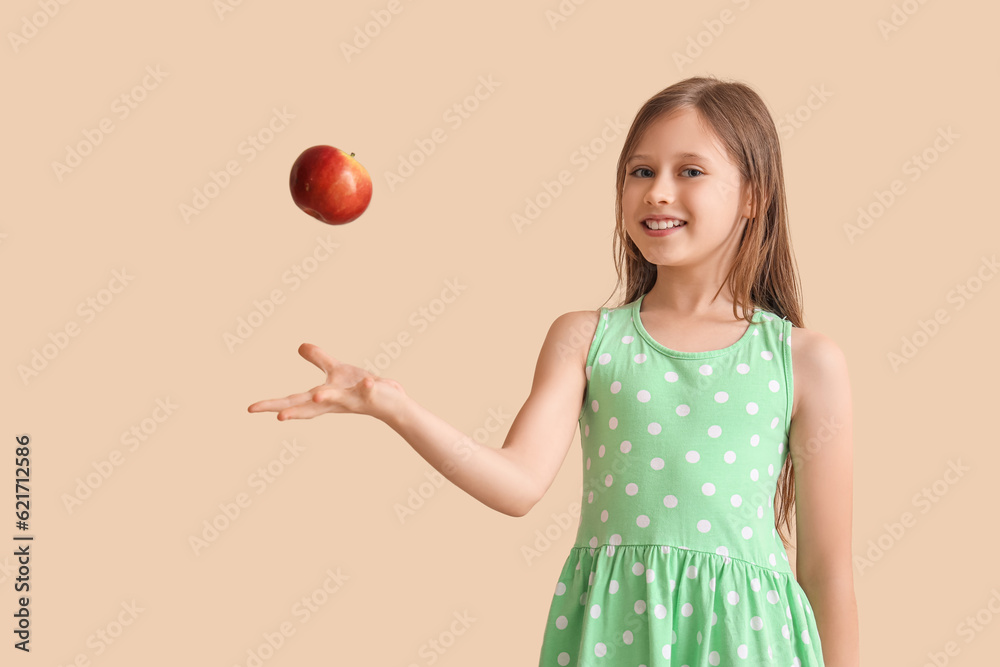 Little girl throwing apple on beige background