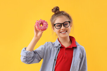 Little girl with tasty doughnut on yellow background