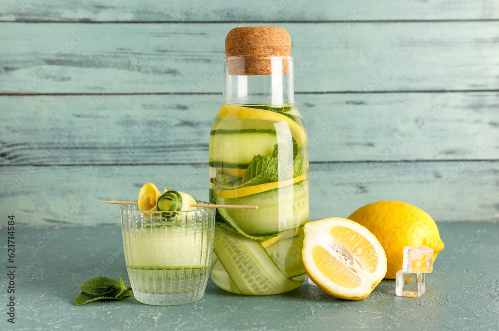Glass and bottle of lemonade with cucumber on blue table