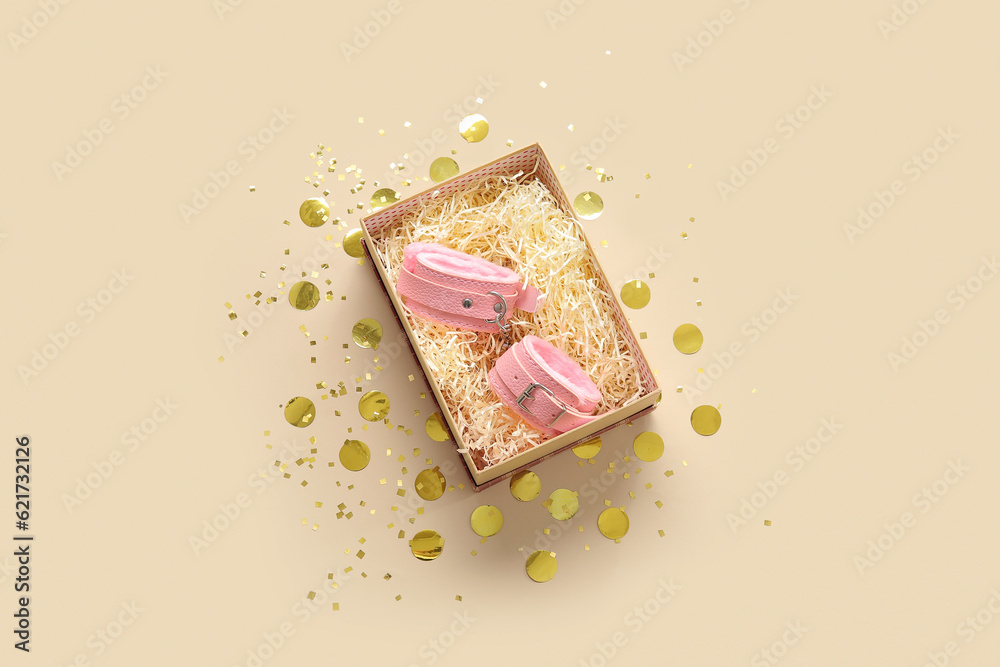Gift box with handcuffs and confetti on beige background