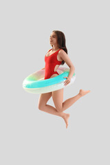 Sticker - Young woman in swimsuit with inflatable ring jumping on light background