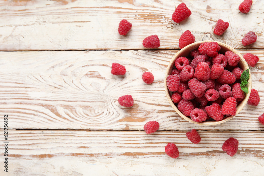 Bowl with fresh raspberry on light wooden background