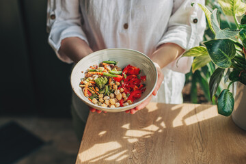 Wall Mural - Young woman eating healthy food sitting in the beautiful interior with green flowers on the background