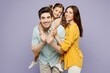 © ViDi Studio - Young cool parents mom dad with child kid daughter girl 6 years old wear blue yellow casual clothes give piggyback ride to joyful, sit on back isolated on plain purple background. Family day concept.