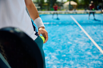 Close up of paddle tennis player about to serve ball during match on outdoor court.