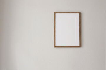 Wall Mural - Vertical wooden picture frame mockup hanging on beige wall. Poster mock-upframe on pastel background in sunlight. Home interior with soft shadow, empty copyspace. Art display concept. Minimal interior