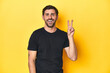 © Asier - Caucasian man in black t-shirt, yellow studio backdrop showing number two with fingers.