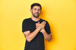 © Asier - Caucasian man in black t-shirt, yellow studio backdrop laughing keeping hands on heart, concept of happiness.