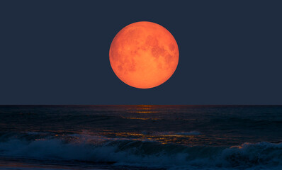 Wall Mural - Night sky with orange moon in the clouds over the calm blue sea 
