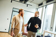 © LIGHTFIELD STUDIOS - cheerful business partners with mobile phones and laptop smiling at each other while talking in contemporary office environment with high tech interior, productivity and cooperation concept