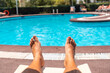 © unai - Men's legs lying on a deck chair overlooking the water, sunbathing by the pool of the hotel resort