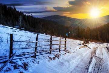 Wall Mural - day and night time change concept. fence on snowy mountain slope near the forest in winter with sun 
