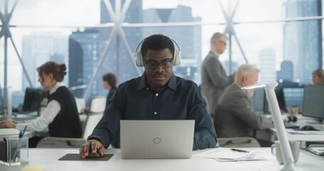 Poster - Succesful Black Man Puts On Headphones And Starts Typing On Laptop Computer In Skyscraper Office In Downtown. Professional Male Software Developer Working On a New Project In Diverse Tech Startup.