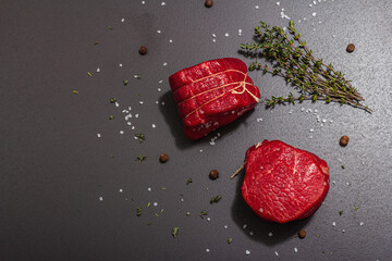 Wall Mural - Raw Ribeye steak with spices and herbs on black stone background. Trendy hard light, dark shadow